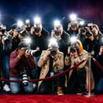 Paparazzi photographers crowd behind a velvet rope on a red carpet with bright camera flashes, symbolizing sudden fame and public attention